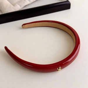 Detailed macro view of deep red patent leather headband with a fine golden metal bow logo