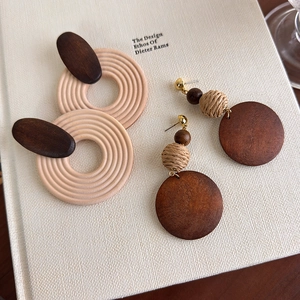 Bohemian geometric wooden earrings with woven straw details on a textured book surface