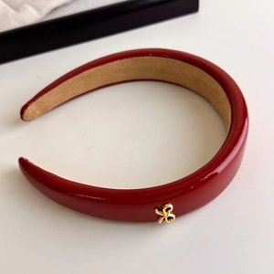 Close-up of a glossy red headband with golden bow detail and soft velvet lining