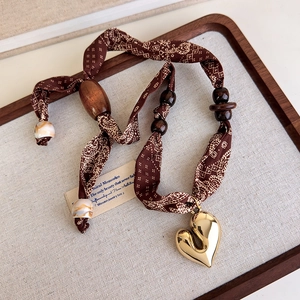 Macro detail of paisley silk scarf necklace with wooden beads and golden heart pendant