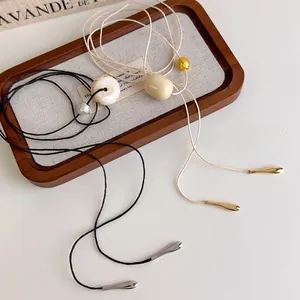 Detail of minimalist ivory pendant necklaces with black and beige cords on a wooden tray