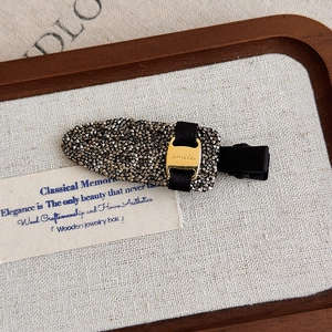 Détail d'une pince à cheveux en strass avec un charme métallique doré gravé smile