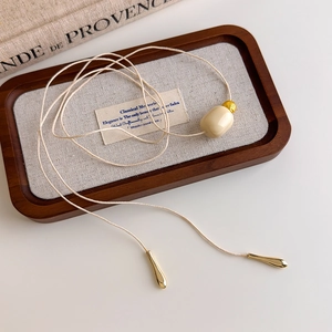 Close-up of minimalist necklace with ivory oval bead and golden bead on linen