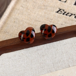 Close-up of leopard print heart earrings on a rustic wood and linen background