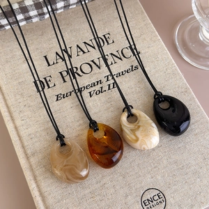 Detail of four resin teardrop pendants in amber and marble patterns on textured book
