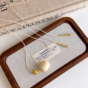 Detailed close-up of ivory ceramic bead and hammered gold bead on a woven minimalist necklace