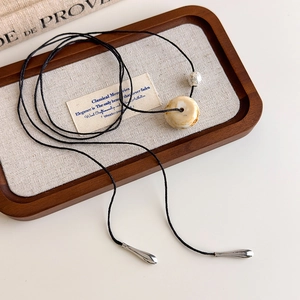 Detail of vintage ivory round bead pendant on black woven long cord with teardrop accents