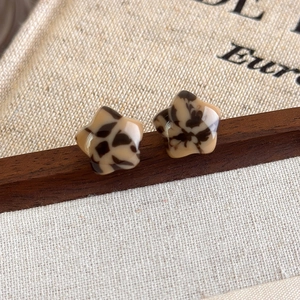 Close-up of leopard print star stud earrings with a glossy finish on vintage wooden base