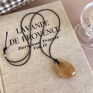 Detail of amber marble resin pendant with black cord on rustic linen texture