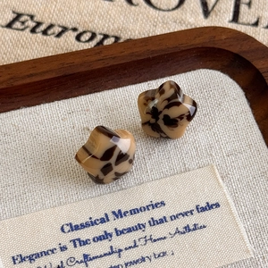 Macro view of leopard print star-shaped resin stud earrings on a linen wooden tray