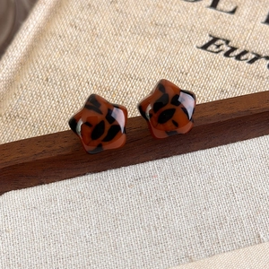 Macro shot of star-shaped leopard print resin earrings on a rustic wooden stand