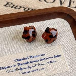 Macro shot of retro leopard print resin earrings on textured beige linen with wood trim