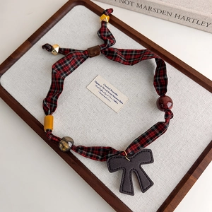 Detalle del collar de tela a cuadros rojos y negros con cuentas y un lazo de cuero negro fino