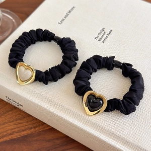 French minimalist black scrunchie set with gold-framed heart pearl charms on a book