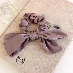 Detail of elegant dusty purple satin bow scrunchie on a vintage linen texture book