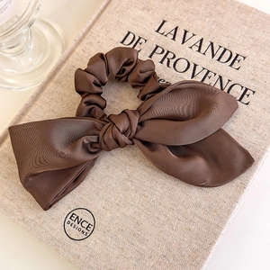 Detailed close-up of dark brown satin bow scrunchie on a textured book surface