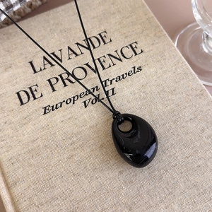 Macro detail of irregular black teardrop pendant necklace on textured linen book page