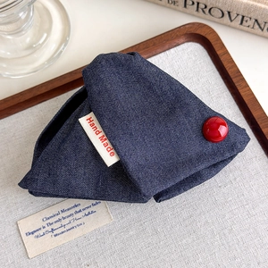 Detail of a navy blue denim triangle pouch with a red button and hand made label