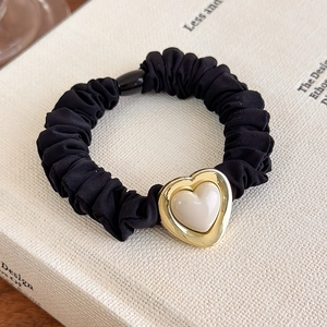 Detail of a black French scrunchie with heart-shaped golden metal and pearl charm detail