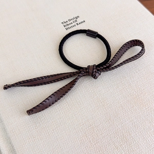 Détail macro de l'élastique à cheveux en cuir marron avec nœud et coutures noires à la main