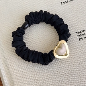 Detail of black pleated scrunchie with a gold-bordered heart charm and creamy texture