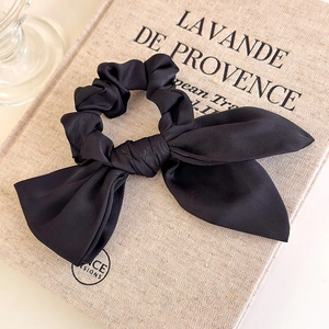 Detail of a chic black satin scrunchie with a long bow on a vintage linen book
