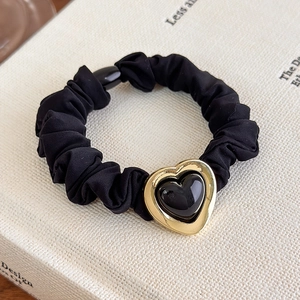 Detail of a black pleated hair scrunchie with a gold heart pendant on a book cover