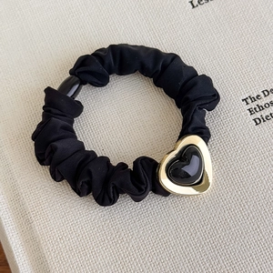 Detail of a black pleated scrunchie featuring a gold and black heart metal charm