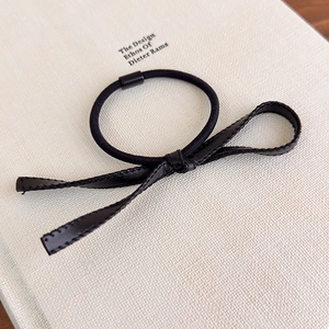 Détail du chouchou nœud en cuir PU noir minimaliste avec corde élastique sur fond de livre
