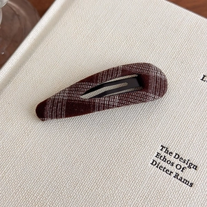 Detail of dark brown vintage plaid fabric BB hair clip on textured book background