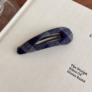 Close-up of minimalist navy blue plaid fabric BB hair clip on a textured book page