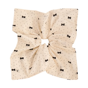 Détail d'un chouchou beige à pois avec motifs nœuds et un pendentif cœur argenté