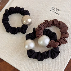 Tre elastici per capelli eleganti con grandi perle nere e marroni su un libro bianco