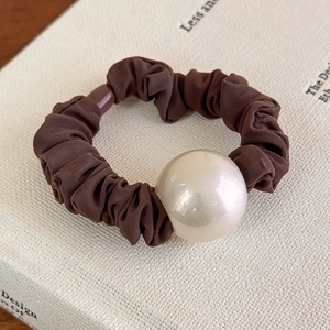 Vista dettagliata di uno scrunchie in chiffon marrone con una grande perla su un libro