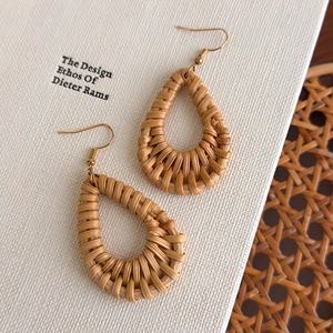 Detail of bohemian rattan teardrop earrings with golden hooks on white fabric