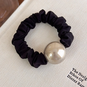 Dettaglio di scrunchie in tessuto nero a pieghe con una grande sfera in metallo dorato
