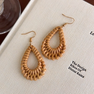Handmade bohemian rattan teardrop earrings with gold metal hooks on white book background