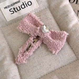 Dettaglio della molletta a fiocco in tweed rosa con strass a cuore e clip in metallo
