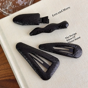 Detail of four-piece black faux leather hair clips with embossed crocodile pattern texture