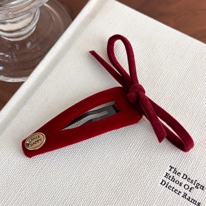 Detail of red velvet bow hair clip with gold Smile Happy charm on a woven background