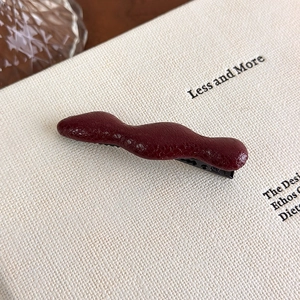 Detailed close-up of dark red wave leather hair clip on a minimalist book cover