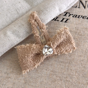 Dettaglio di un fermaglio per capelli a fiocco peluche kaki con strass a cuore e clip