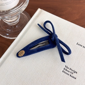 Detail of dark blue velvet bow hair clip with a gold metal 'SMILE HAPPY' logo tag