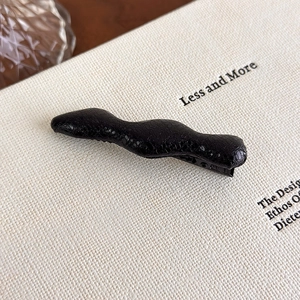 Close-up of wavy black hairpin with premium faux leather texture on a minimal background