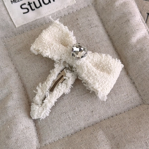 Dettaglio ravvicinato del fermaglio a fiocco in tweed crema con strass a forma di cuore