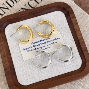 Macro detail of gold and silver irregular wave C-shape hoop earrings in a wooden tray
