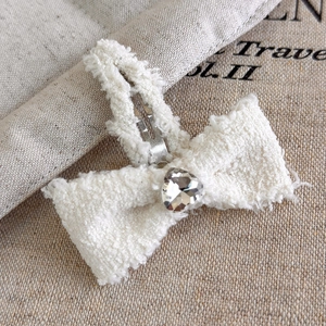 Dettaglio del fermaglio a fiocco in peluche crema con strass a cuore e clip metallica