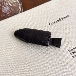 Detail shot of black faux leather hair clip with crocodile pattern texture on a white book