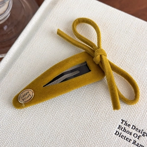 Detail of mustard yellow velvet bow hair clip with gold Happy Smile metal label