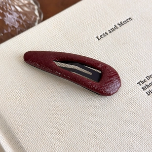 Close-up of wine red faux leather hair clip with crocodile skin texture on a book